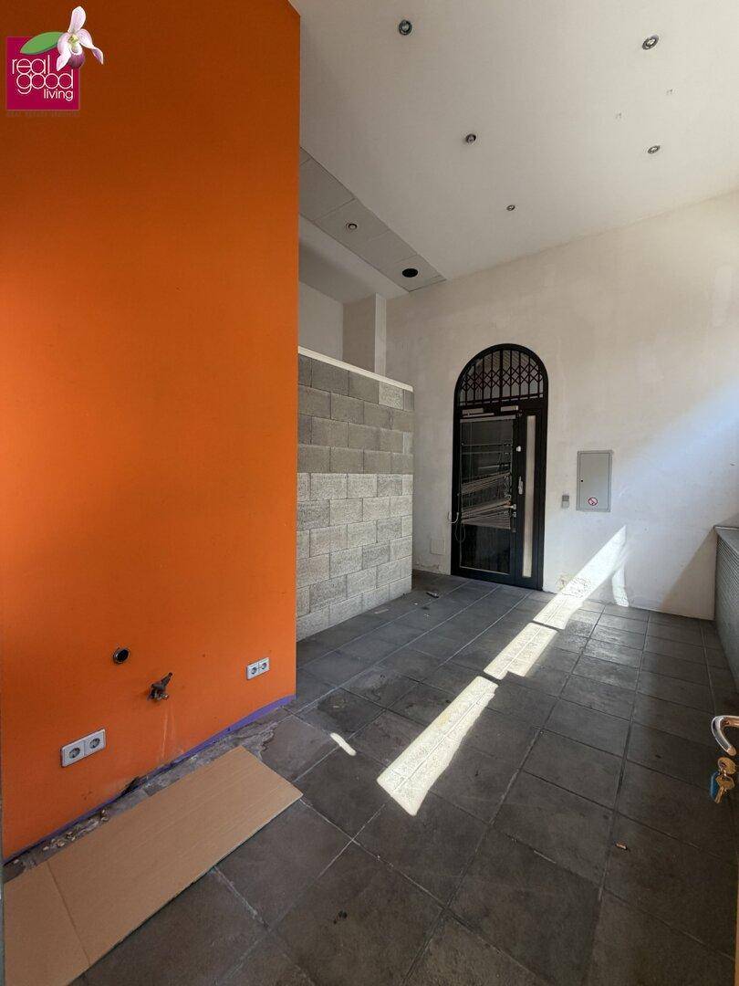 Eingangsbereich eines Gewerberaums mit Fliesenboden, orangefarbener Wand und einem Bogenfenster.