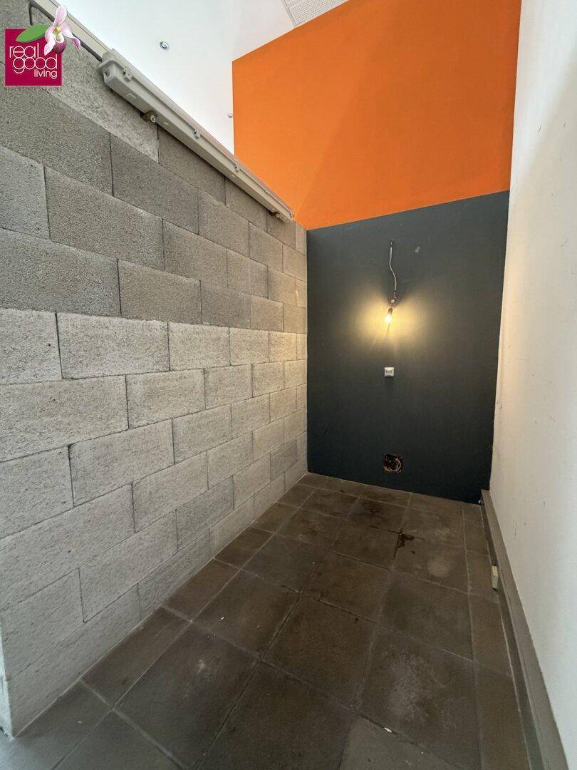 Schmaler Raum mit Fliesenboden, unverputzten Ziegelwänden und einer dunklen Akzentwand.