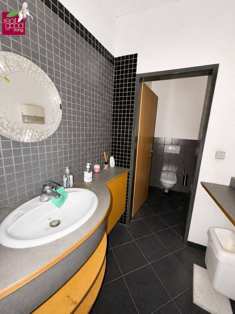 Modernes Badezimmer mit grau-schwarzen Fliesen, ovalem Waschbecken und rundem Spiegel.