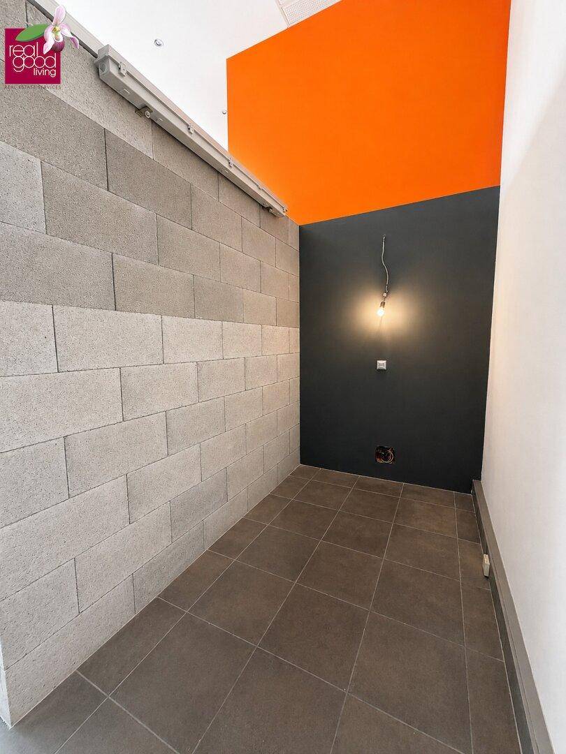 Schmaler Raum mit Fliesenboden, unverputzten Ziegelwänden und einer dunklen Akzentwand.