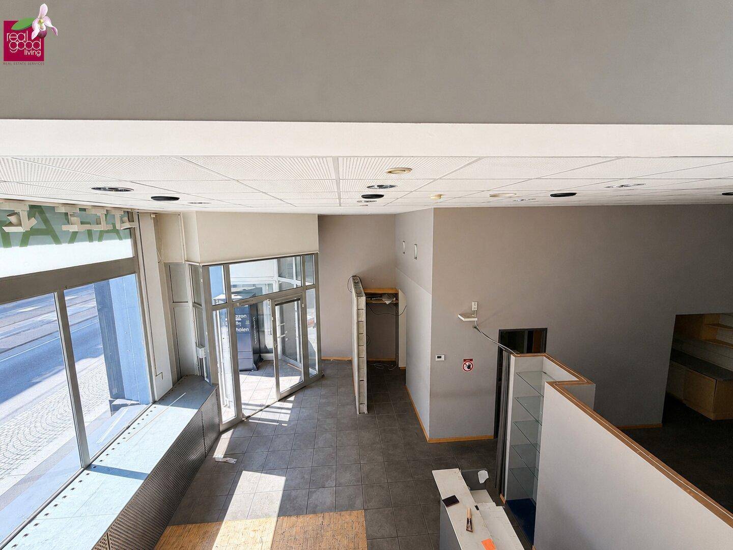 Großer Gewerberaum mit hohen Decken, Fliesenboden und breiter Glasfront zum Eingangsbereich.