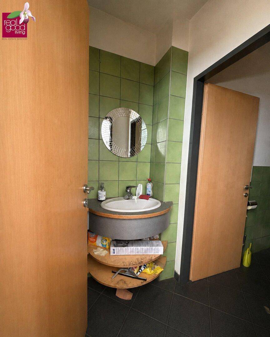 Badezimmer mit grün gefliesten Wänden, ovalem Waschbecken und Holzregalen unter dem Waschtisch.