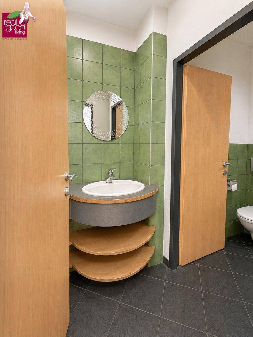 Badezimmer mit grün gefliesten Wänden, ovalem Waschbecken und Holzregalen unter dem Waschtisch.