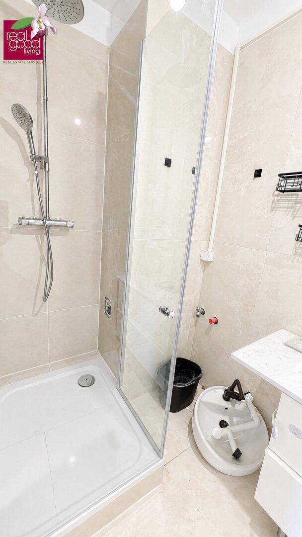 Modernes Badezimmer mit begehbarer Dusche, Regenduschkopf und hellen Fliesen.