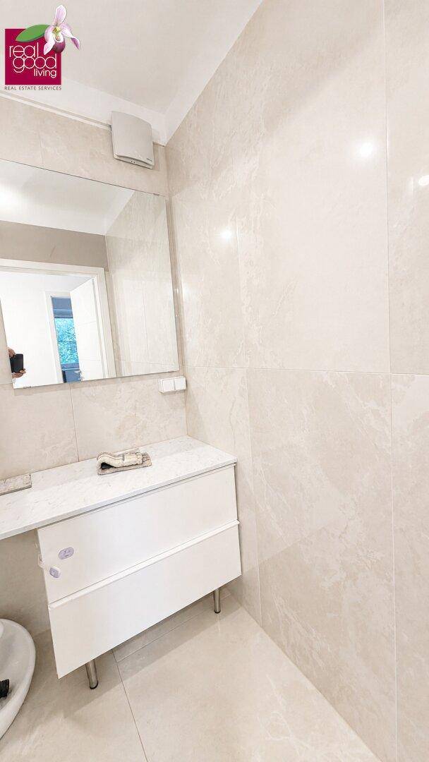 Badezimmer mit modernem Waschtischunterschrank, großem Spiegel und hellen Wandfliesen.