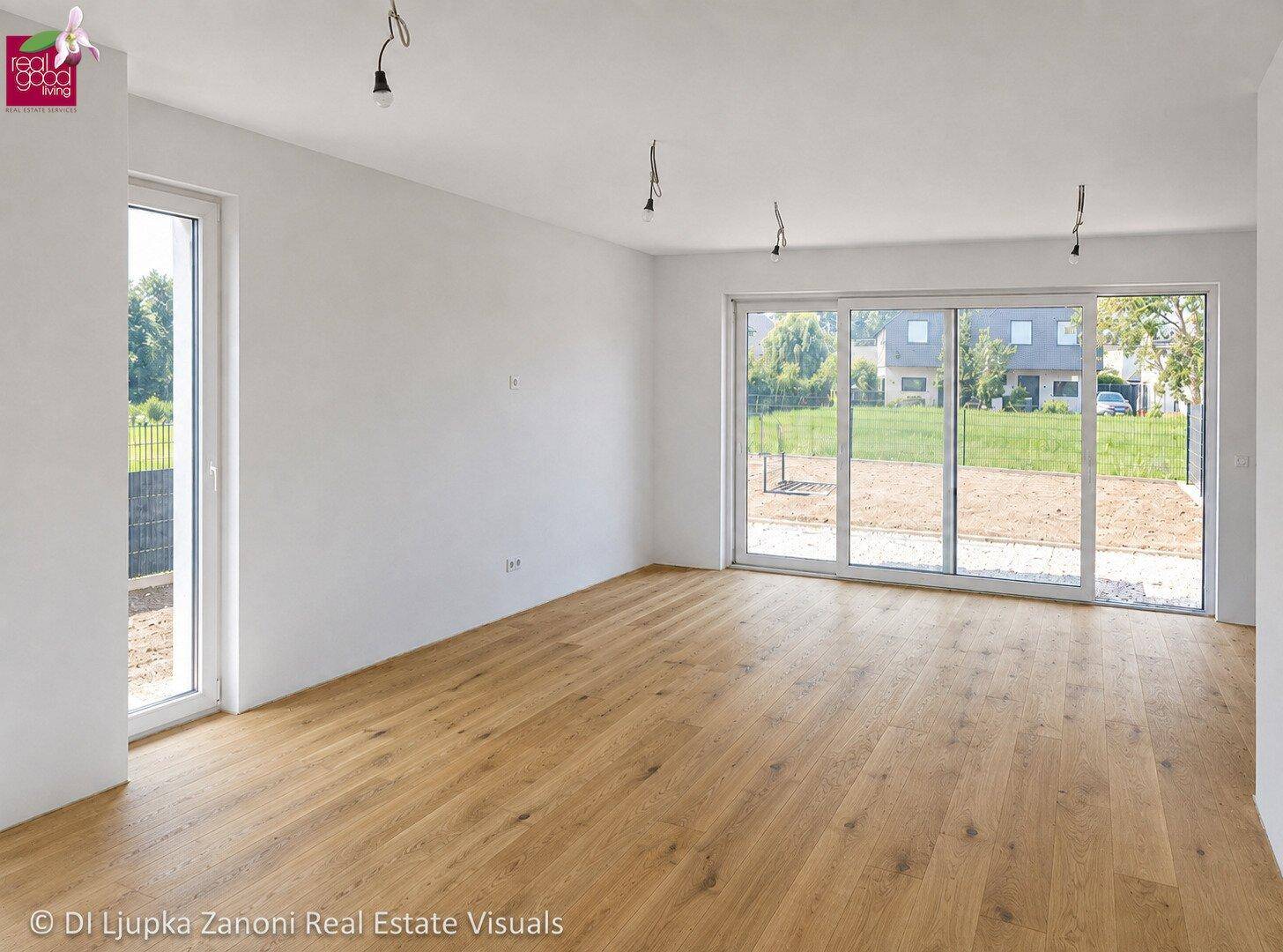 Heller, leerer Wohn-Essbereich mit Holzboden und großer Schiebetür zur zukünftigen Terrasse.