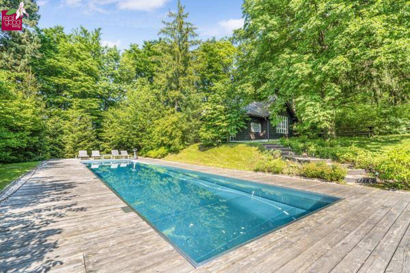 Großer Außenpool mit Holzdeck, umgeben von üppiger grüner Landschaft.