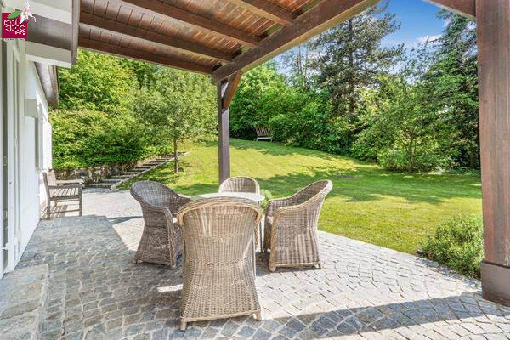 Überdachte Terrasse mit Korbmöbeln und Blick auf den weitläufigen Garten.
