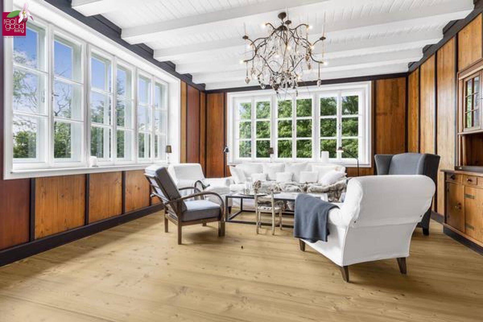 Gemütliches Wohnzimmer mit Holzwänden, Holzbalkendecke und großen Fenstern.