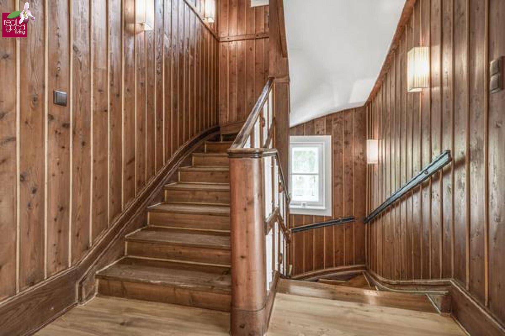Holzvertäfelte Treppe mit elegantem Geländer, die zu den oberen Etagen führt.