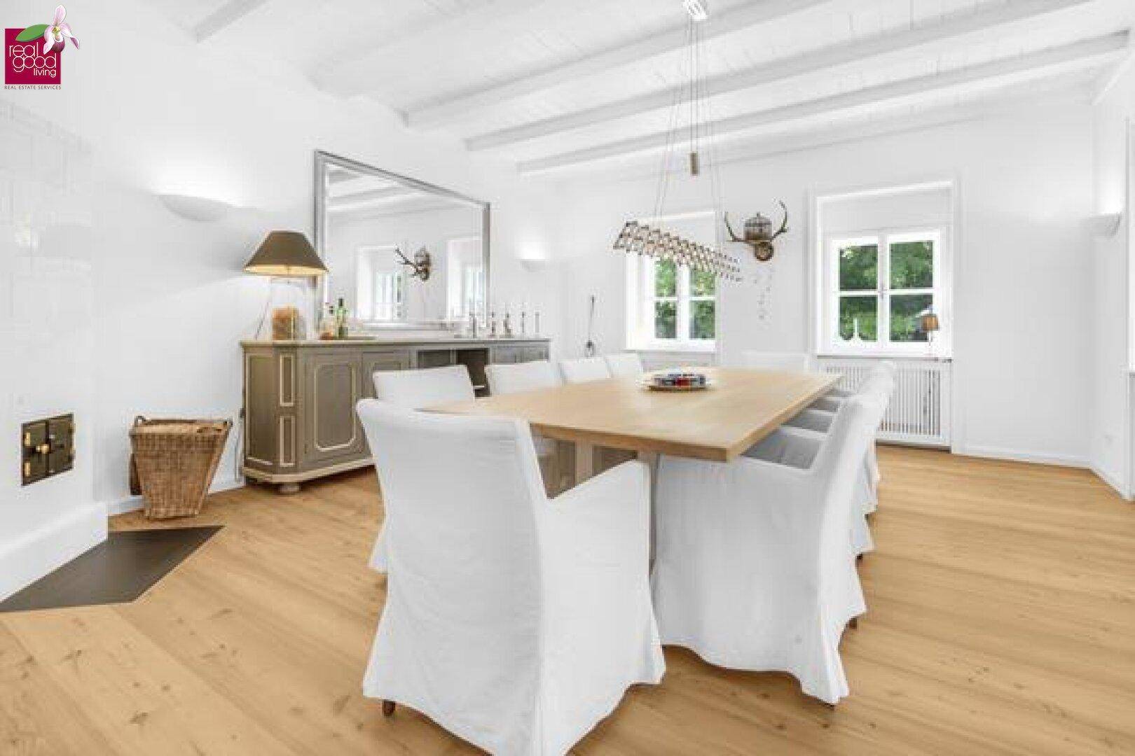 Eleganter Essbereich mit großem Holztisch, weißen Stühlen und Kachelofen.