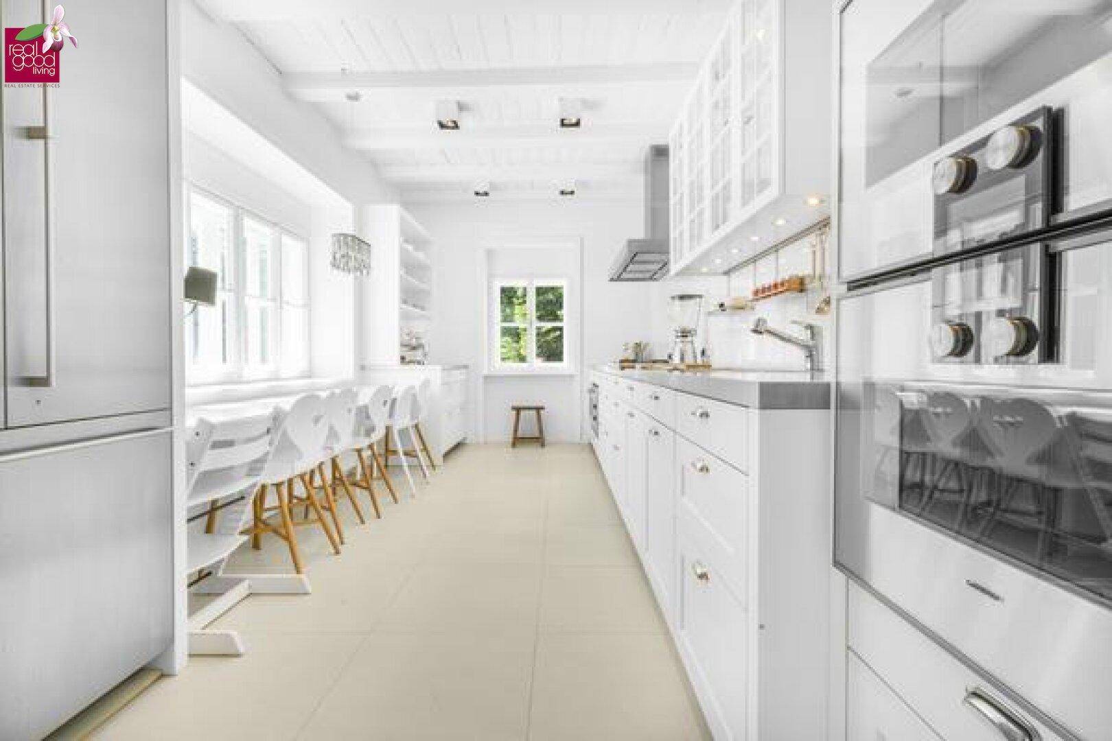 Moderne, helle Küche mit weißen Schränken, integrierten Geräten und Essbereich.
