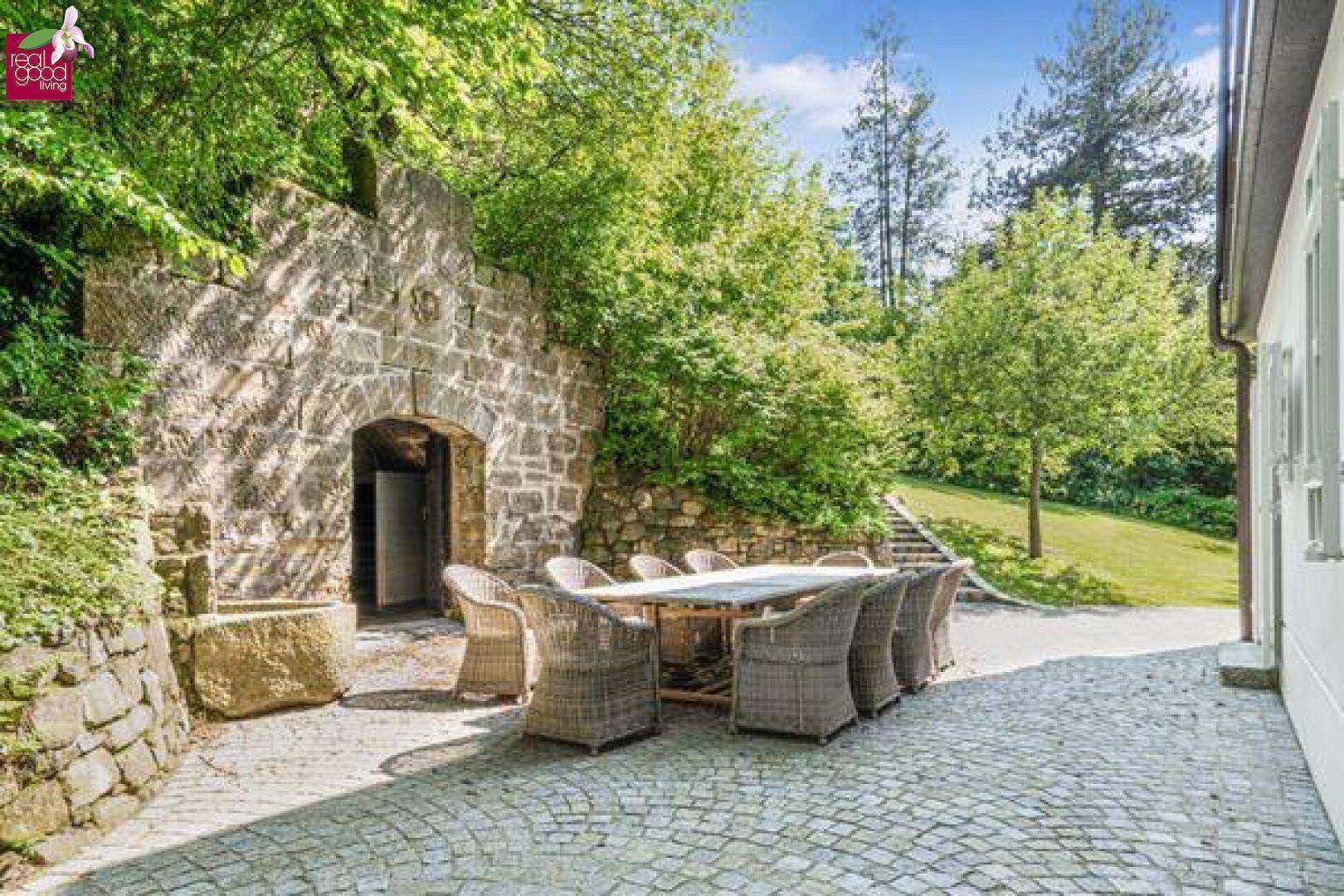 Große Steinterrasse mit Esstisch und Blick auf den Garten und die Natur.