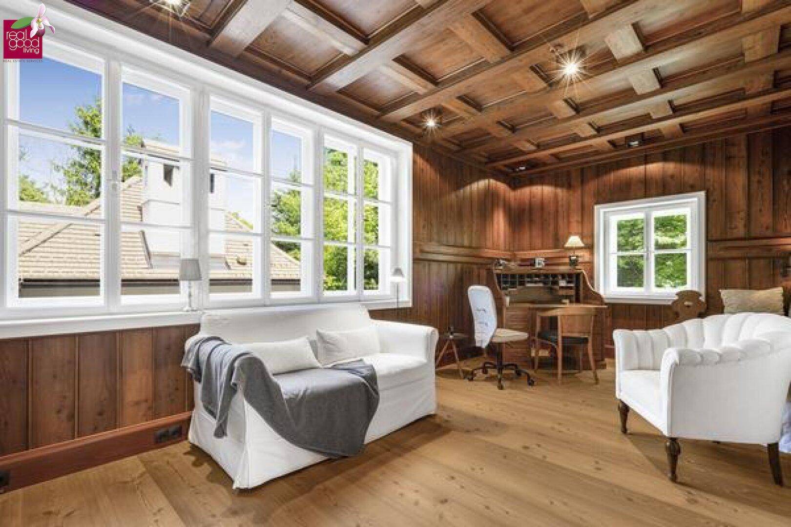Helles Wohnzimmer mit Holzwänden, Holzboden und großen Fenstern.