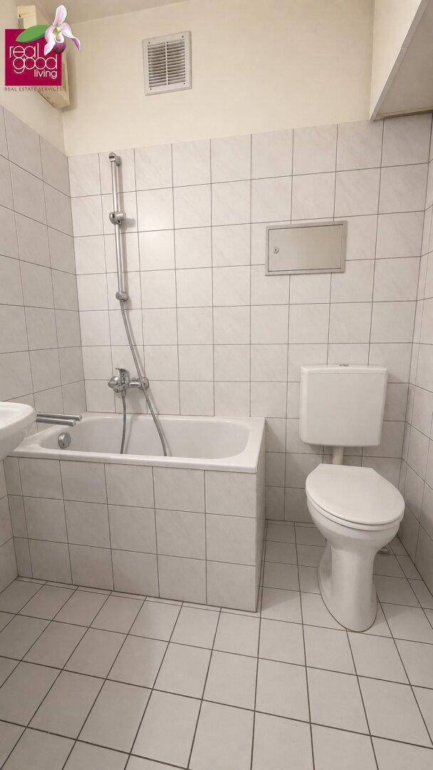 Badezimmer mit weißen Fliesen, Badewanne mit Duschfunktion und Toilette.