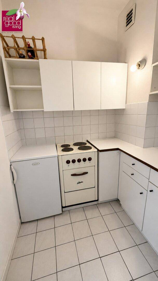 Kleine Küche mit weißen Fliesen, Einbauschränken, Elektroherd und Kühlschrank.