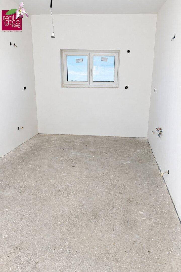 Unmöblierter Raum mit Fenster und Betonboden, bereit für individuelle Gestaltung.