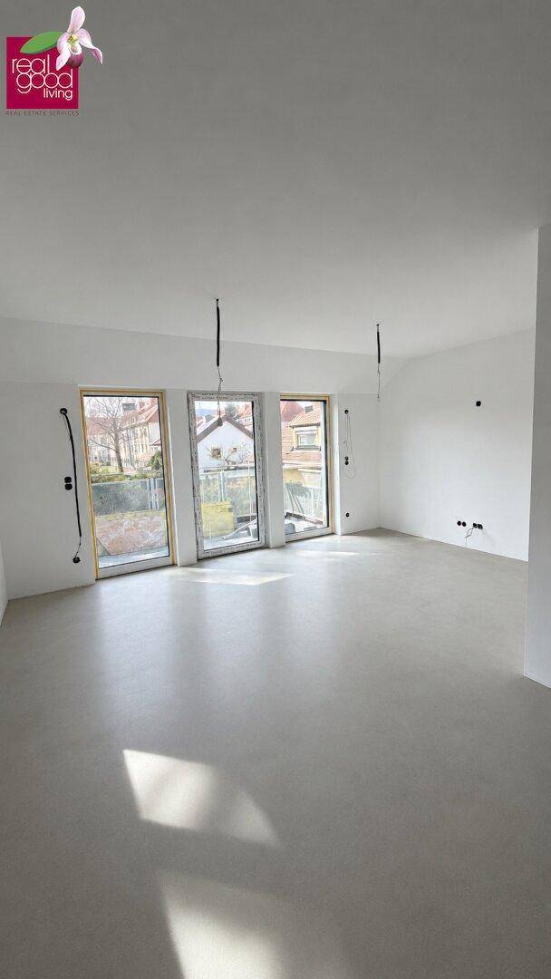 Heller, unmöblierter Raum mit großen Fenstern und Zugang nach draußen, bereit für den Ausbau.