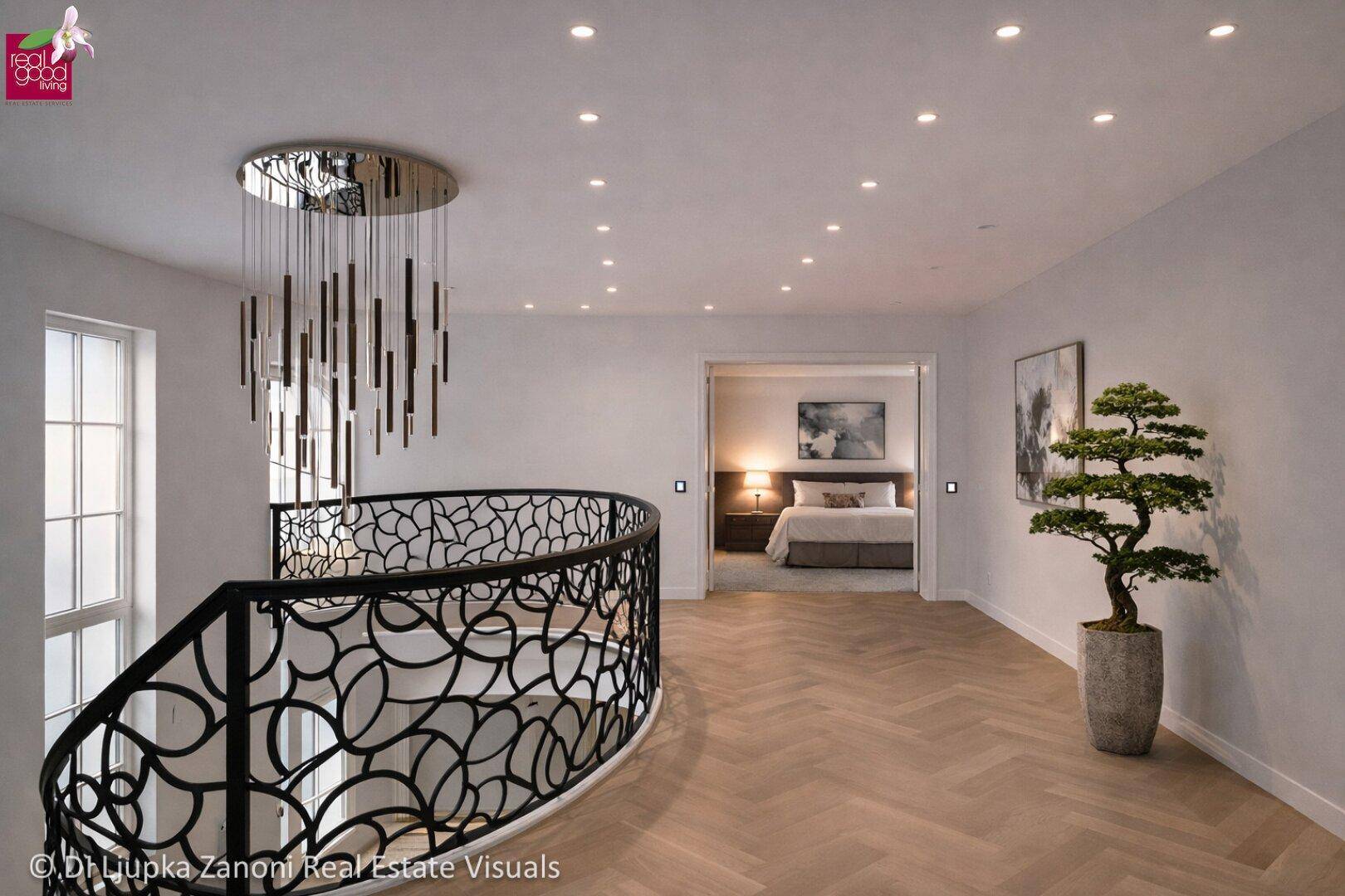 Heller Flur im Obergeschoss mit eleganter Treppe, Kronleuchter und Blick in ein Schlafzimmer.