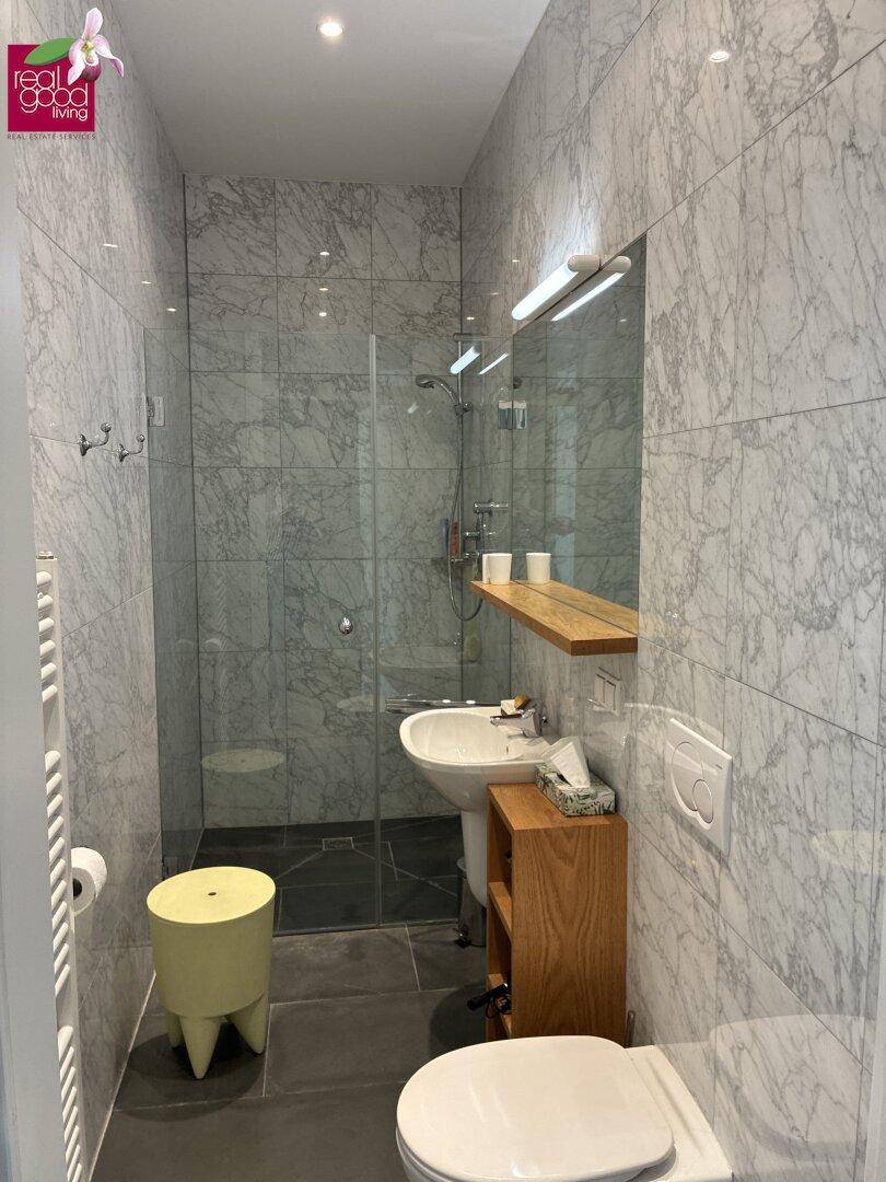 Modernes Badezimmer mit Marmorfliesen, begehbarer Dusche und minimalistischem Design.
