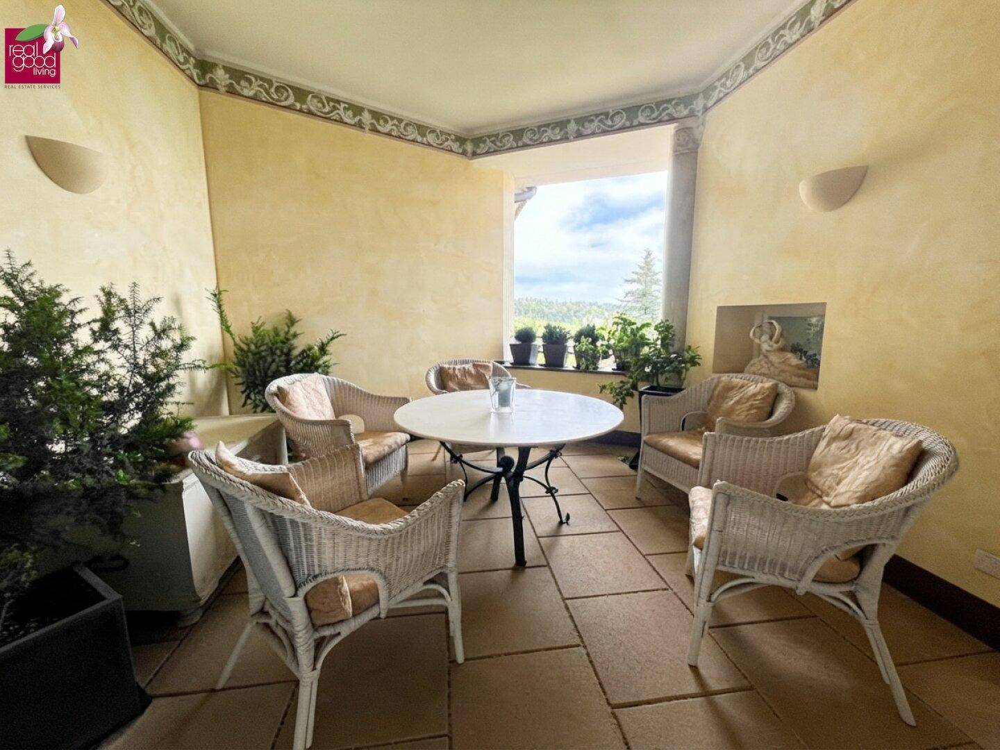 Gemütliche Loggia mit Korbmöbeln, Pflanzen und weitem Blick ins Grüne.