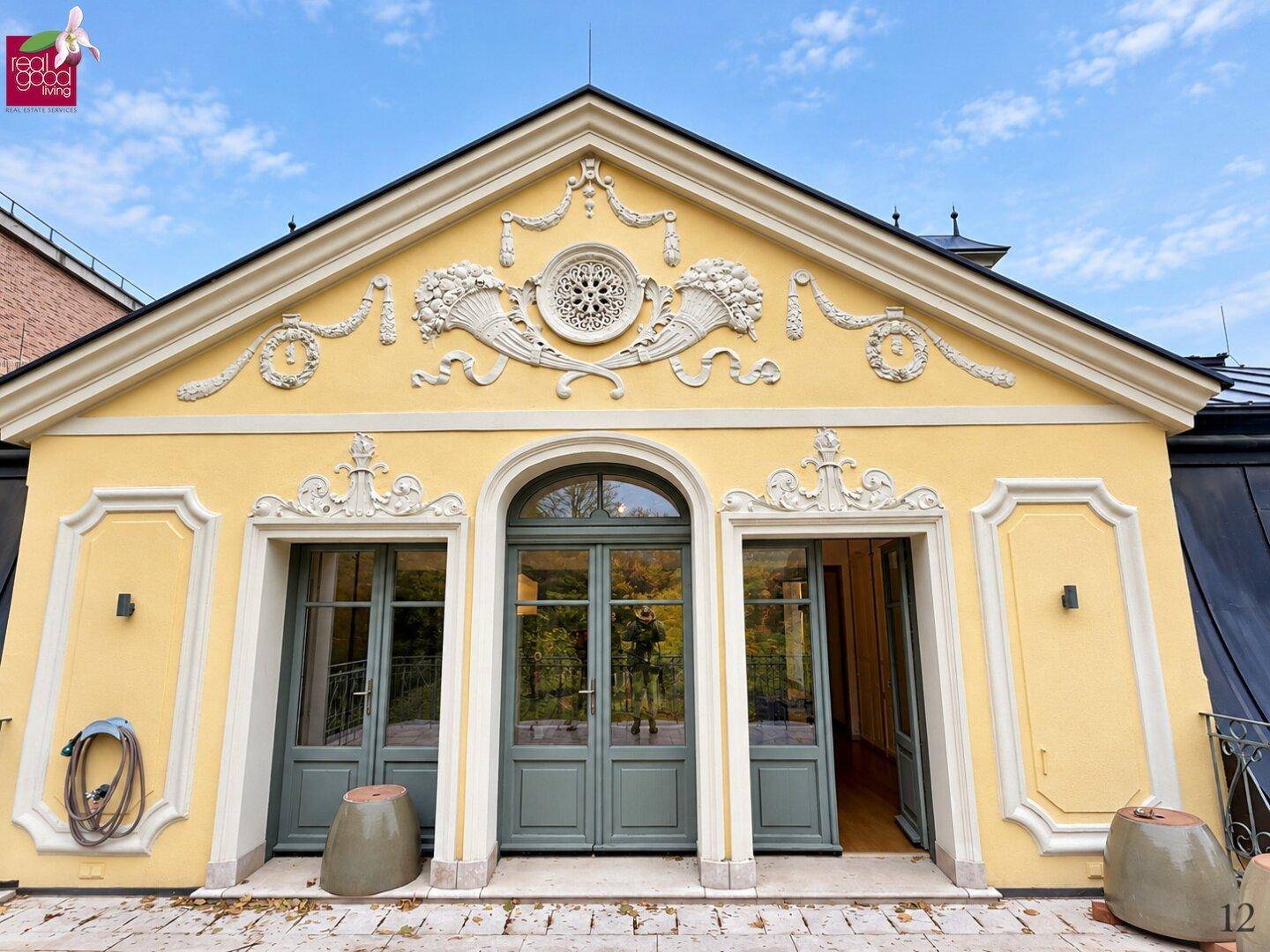 Detailansicht der gelben Fassade mit kunstvollen Stuckverzierungen und großen, eleganten Glastüren.