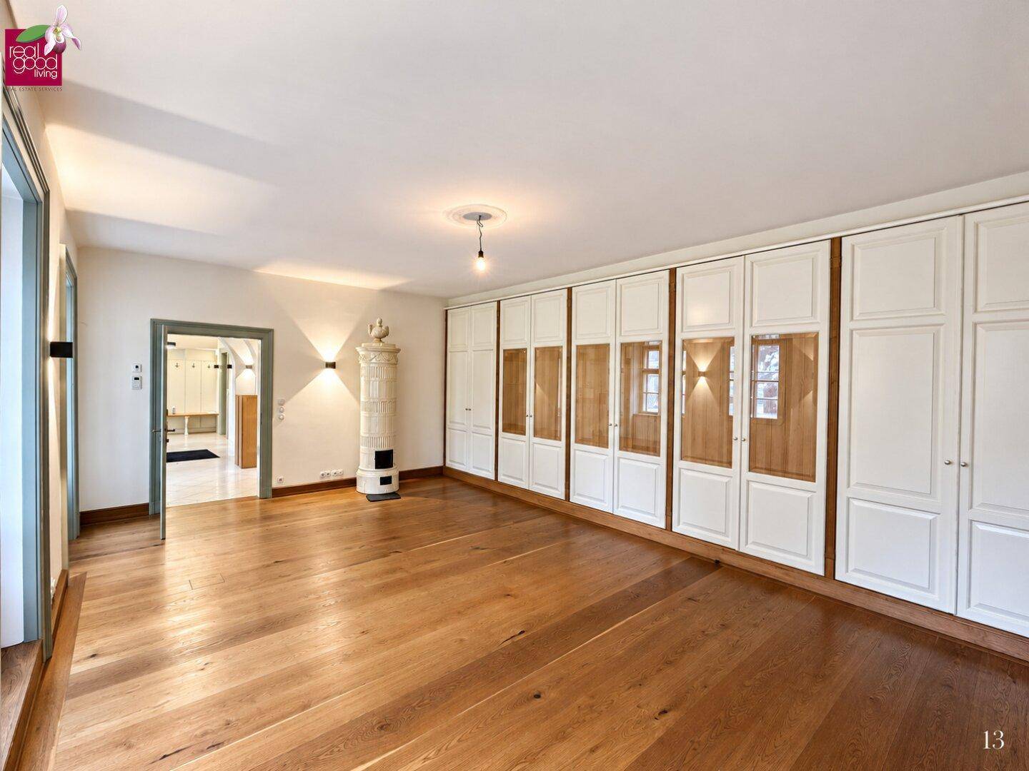 Geräumiges Zimmer mit hellem Holzplankenboden, Einbauschränken und einem traditionellen Kachelofen.