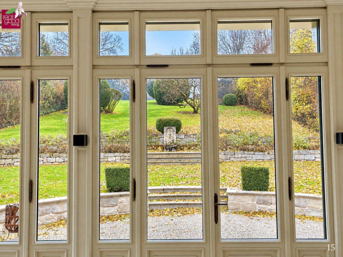 Heller Innenraum mit großen Fenstern, die einen weiten Blick auf den herbstlichen Garten und die Landschaft bieten.