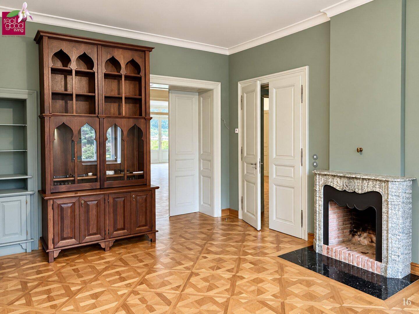 Elegantes Wohnzimmer mit gemustertem Parkettboden, grün gestrichenen Wänden und einem dekorativen Kamin.