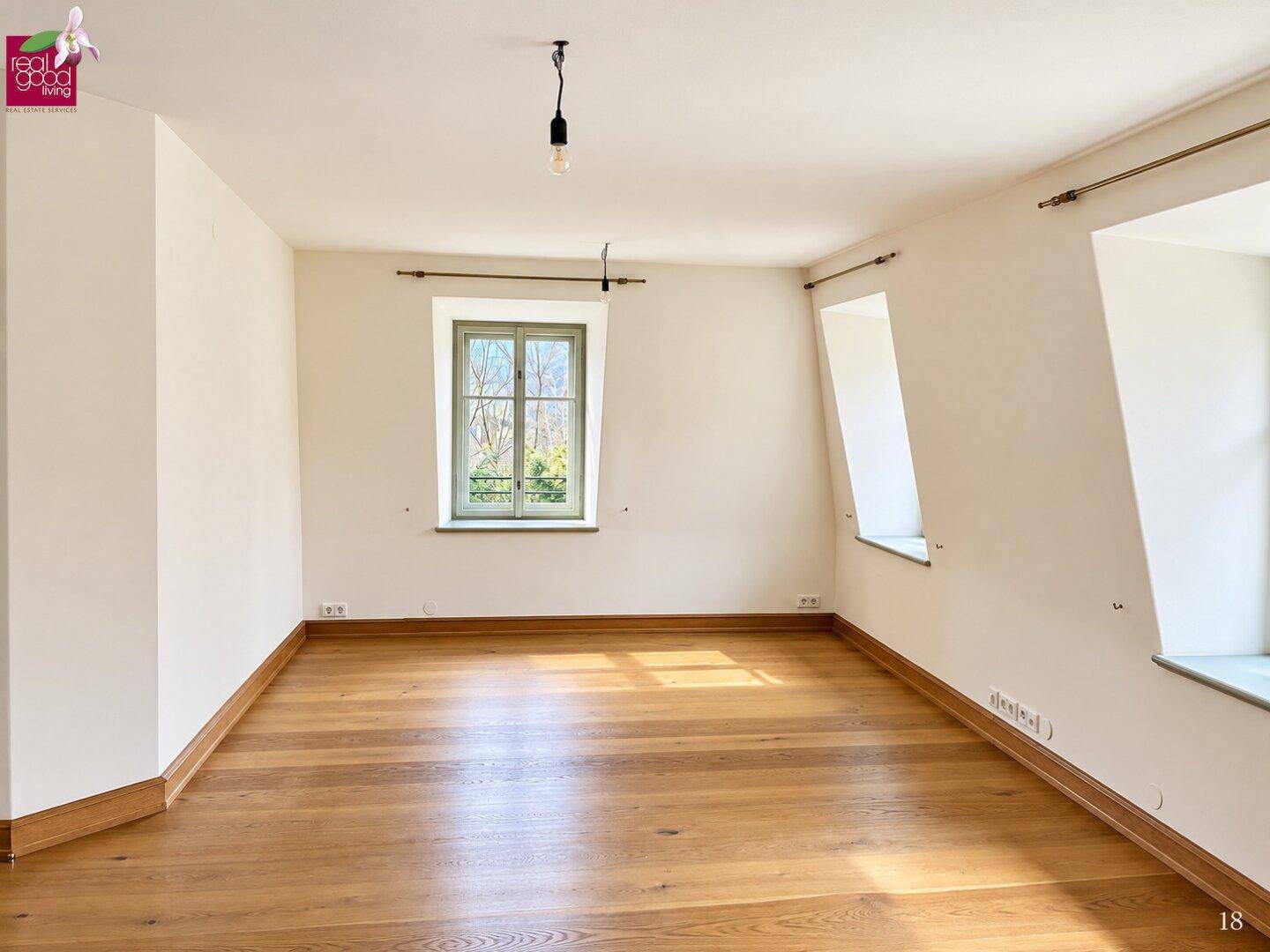 Leeres Zimmer mit hellem Holzplankenboden, weißen Wänden und einem Fenster, teilweise mit Dachschräge.