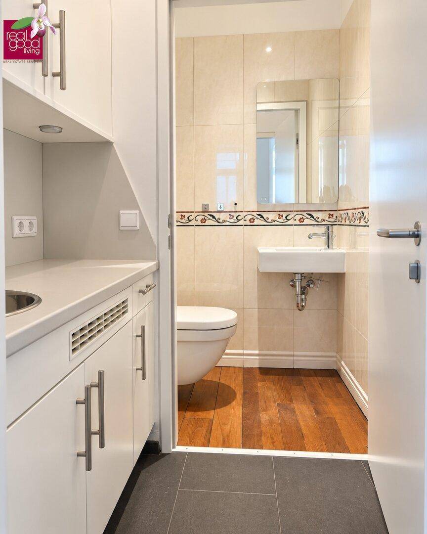 Funktionaler WC-Bereich mit Wand-WC, Waschbecken und einer kleinen Küchenzeile mit Spüle und Unterschränken.
