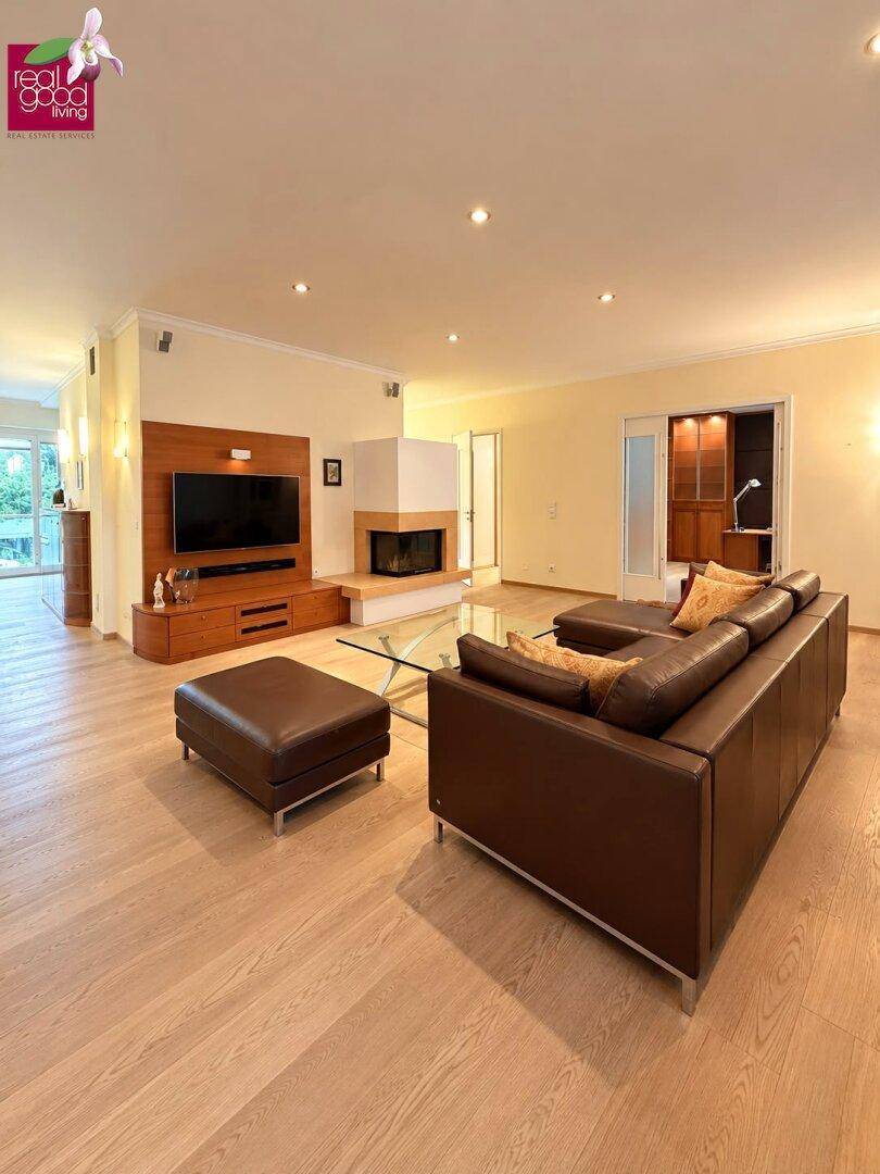 Gemütliches Wohnzimmer mit Kamin, Holzboden und braunen Ledersofas, hell beleuchtet.