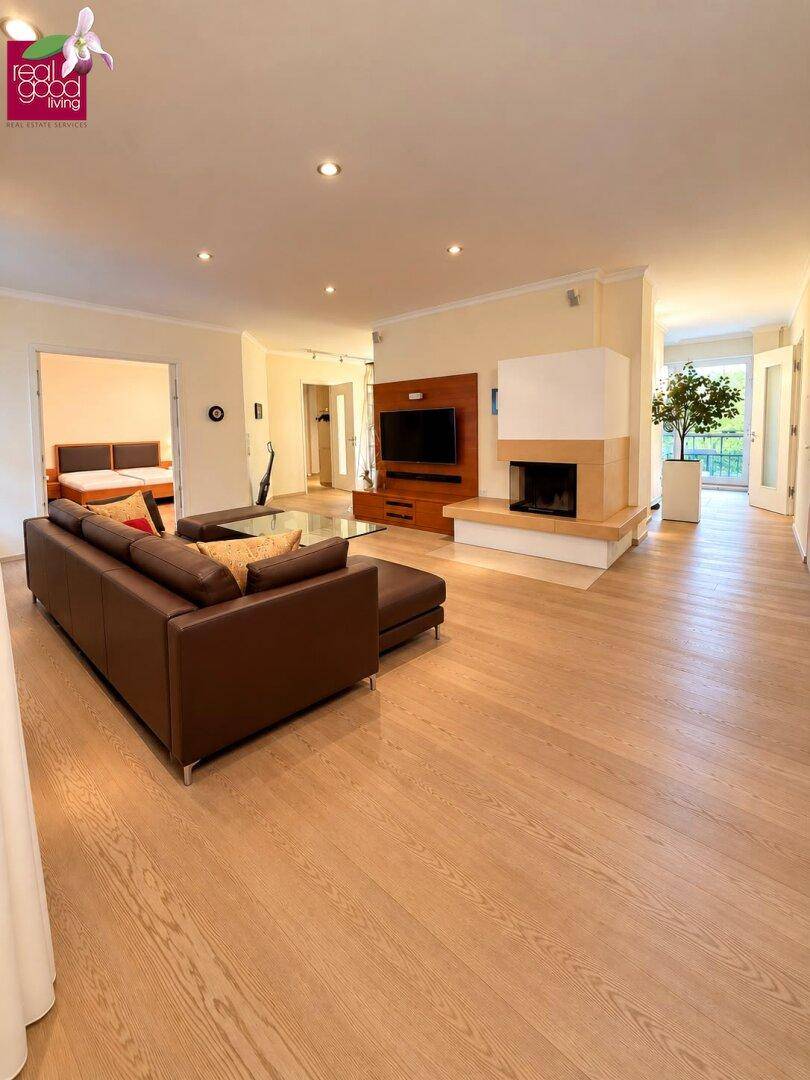 Geräumiges Wohnzimmer mit hellem Holzboden, Kamin und Zugang zu weiteren Räumen.