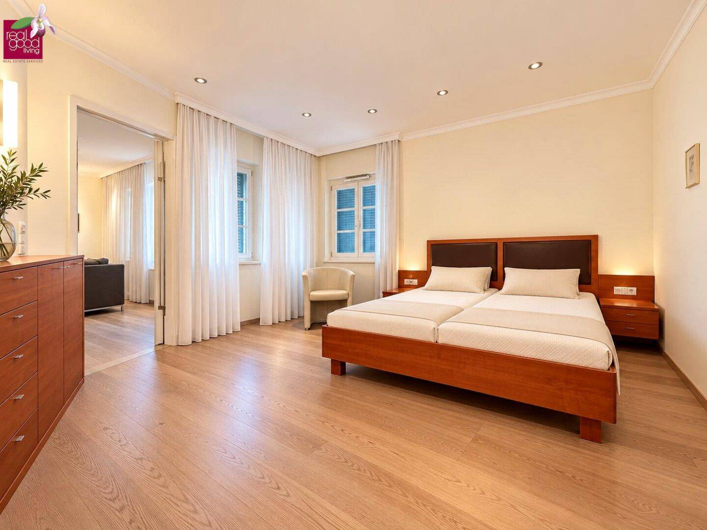 Helles Schlafzimmer mit Holzbett, Nachttischen und hellem Holzboden, gut beleuchtet.