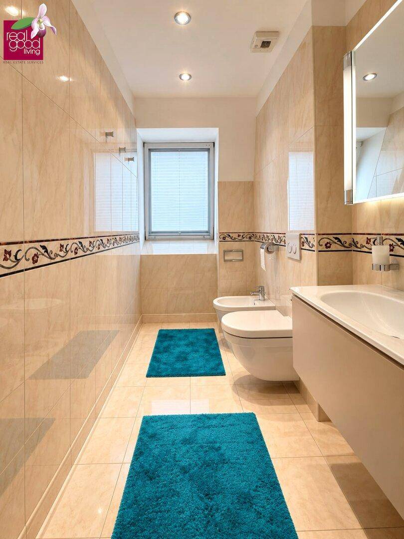 Helles Badezimmer mit Fenster, Bidet, Wand-WC und beigefarbenen Fliesen.