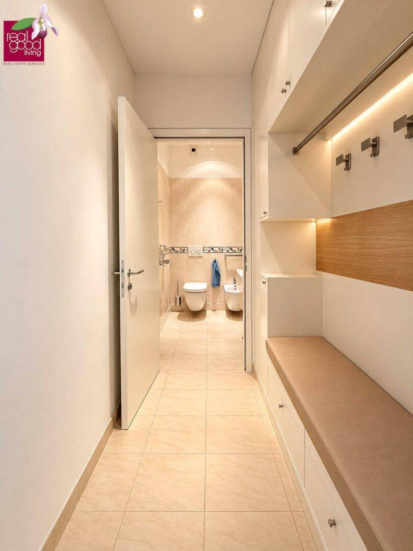 Eingangsbereich mit Garderobe, Sitzbank und Zugang zu einem Badezimmer mit Fliesenboden.