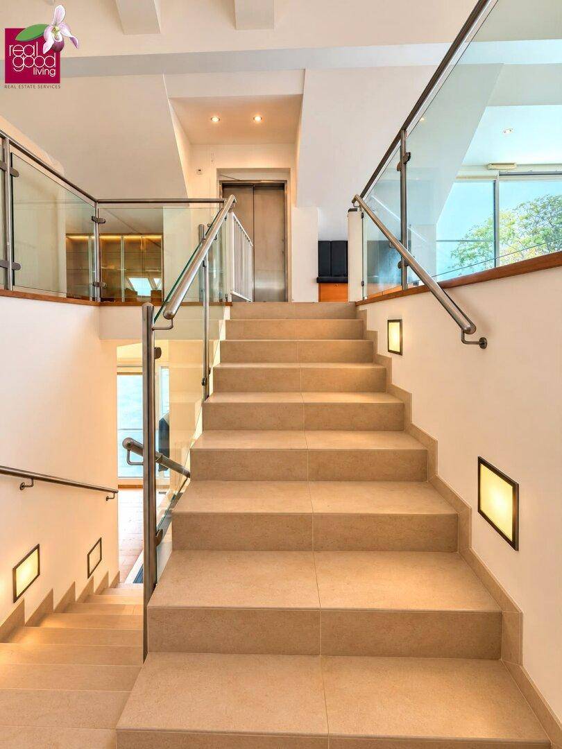 Elegantes Treppenhaus mit Glasgeländer, Fliesenstufen und integriertem Aufzug.