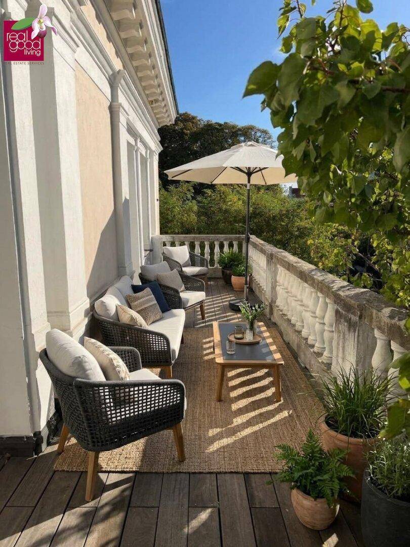 Einladender Balkon mit bequemen Sitzgelegenheiten, Sonnenschirm und Pflanzen für entspannte Momente.