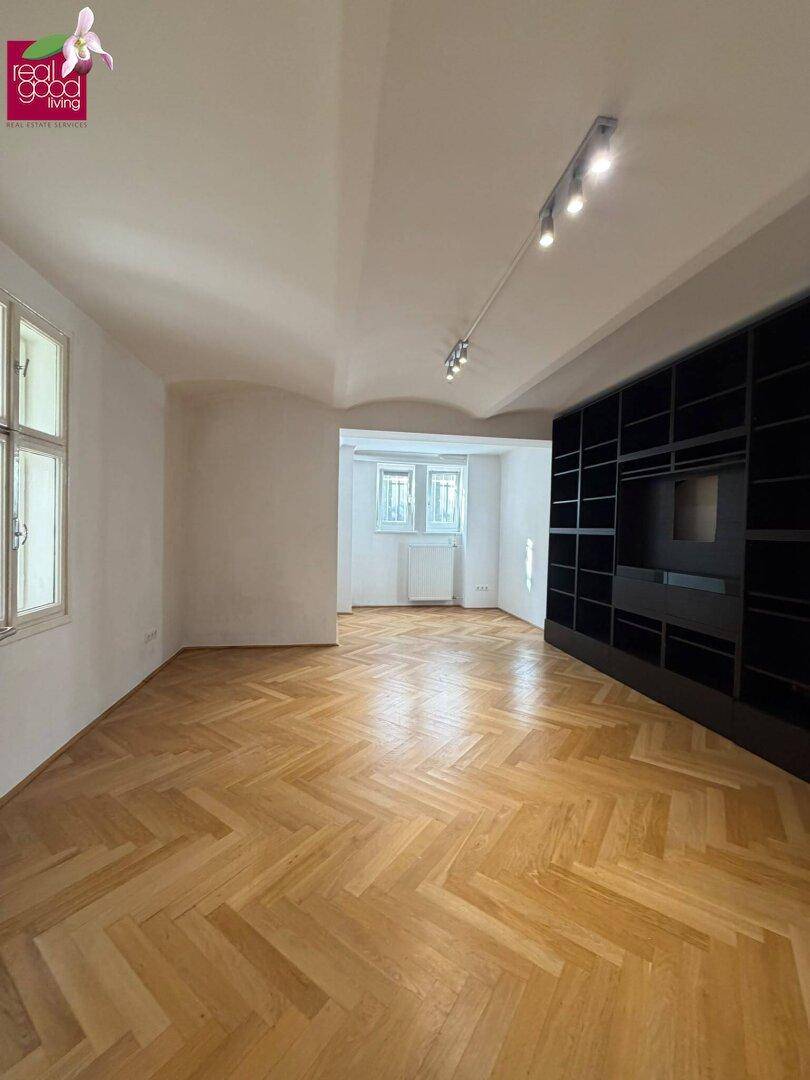 Heller Raum mit Fischgrätparkett und einer großen schwarzen Einbauregalwand.