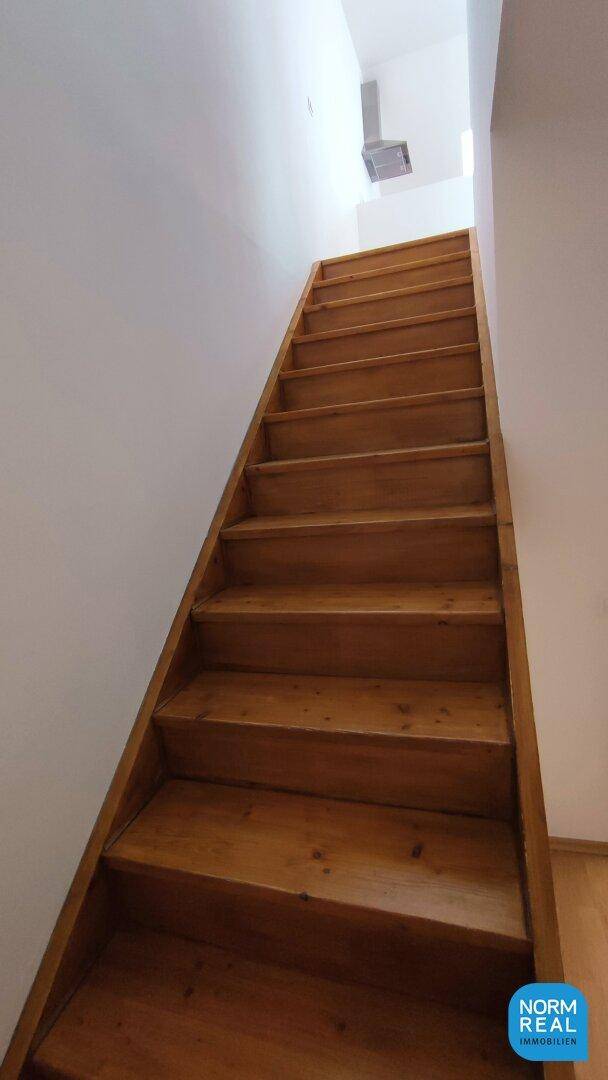 Aufsteigende Holztreppe mit schlichten weißen Wänden, die zu den oberen Räumen führt.