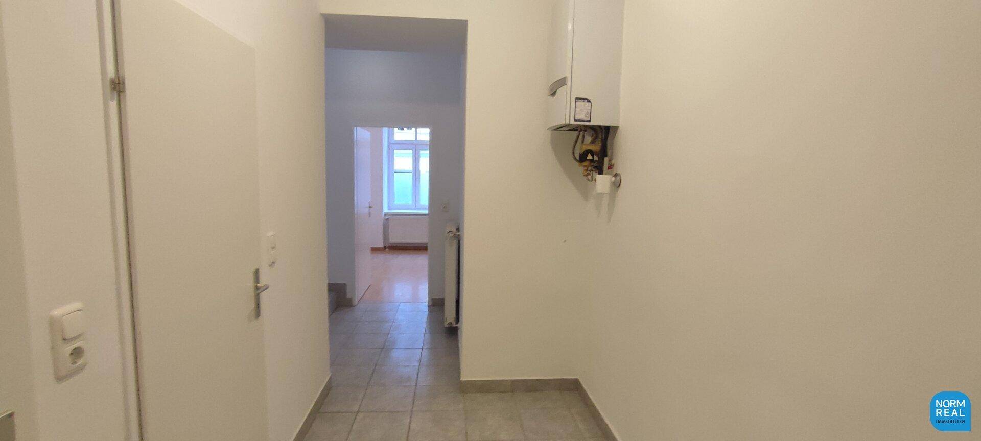 Heller Flur mit Fliesenboden und Wandheizung, führt zu weiteren Zimmern der Wohnung.