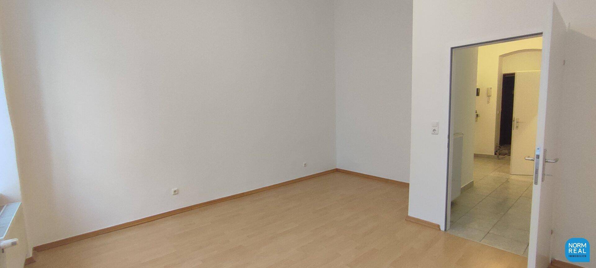 Heller Wohnraum mit Parkettboden und Zugang zu einem gefliesten Flurbereich.