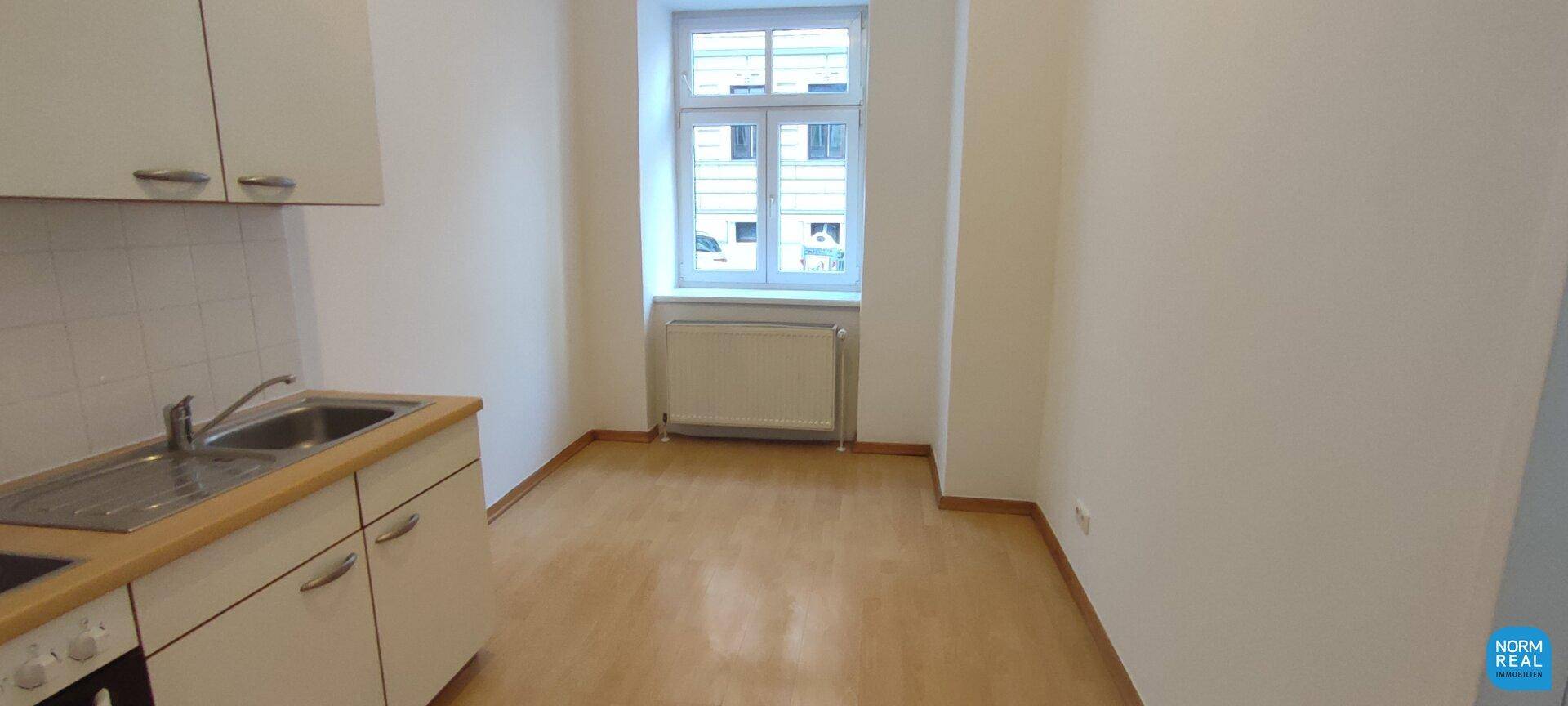 Helle Küche mit Einbauzeile, Fenster und Parkettboden, bietet Platz für einen kleinen Essbereich.