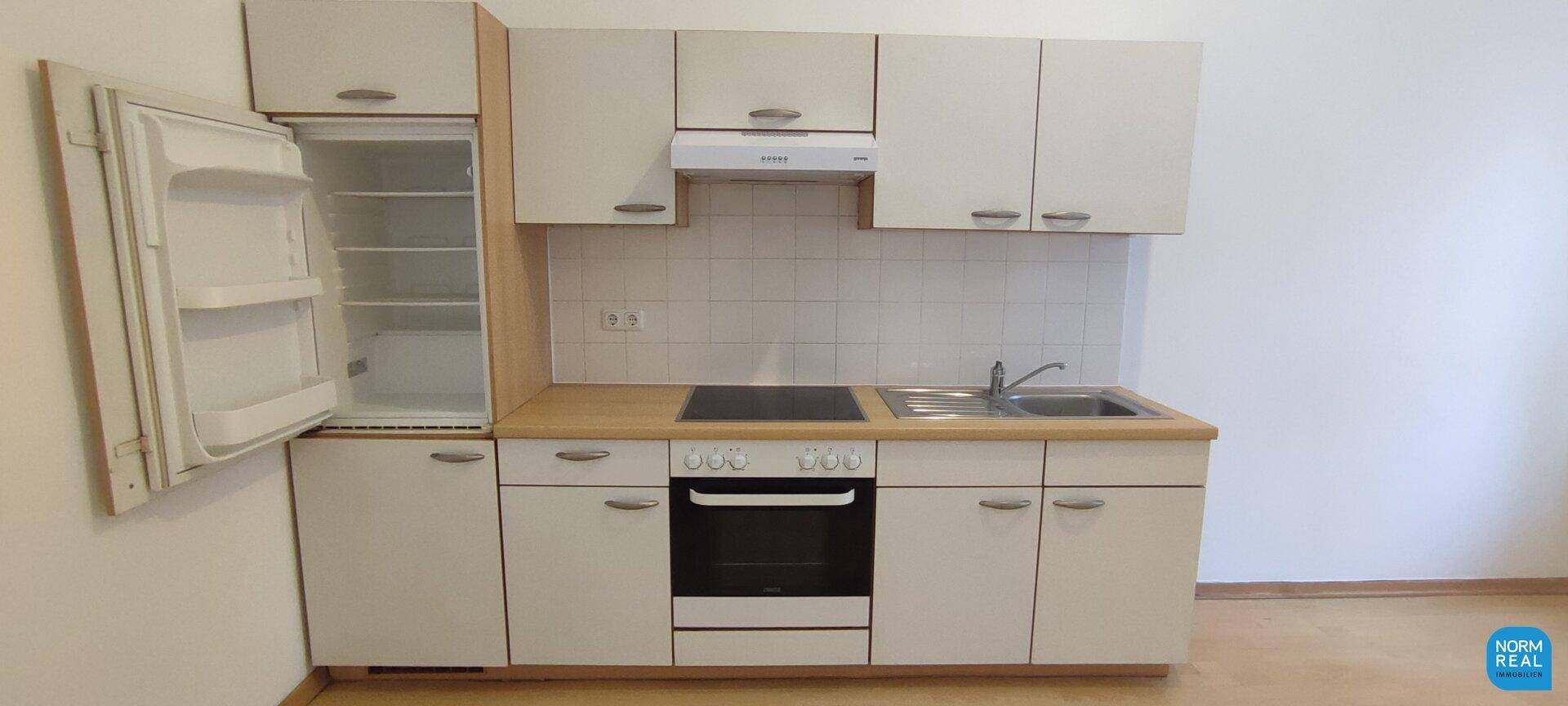 Funktionale Einbauküche mit weißen Schränken, Herd, Backofen und integriertem Kühlschrank.
