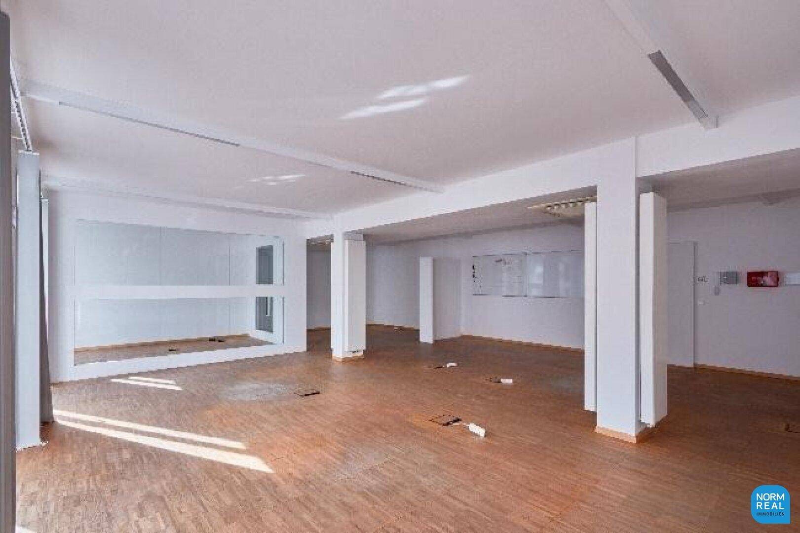 Heller Büroraum mit Holzboden und weißen Wänden, bietet flexible Gestaltungsmöglichkeiten für Arbeitsplätze.