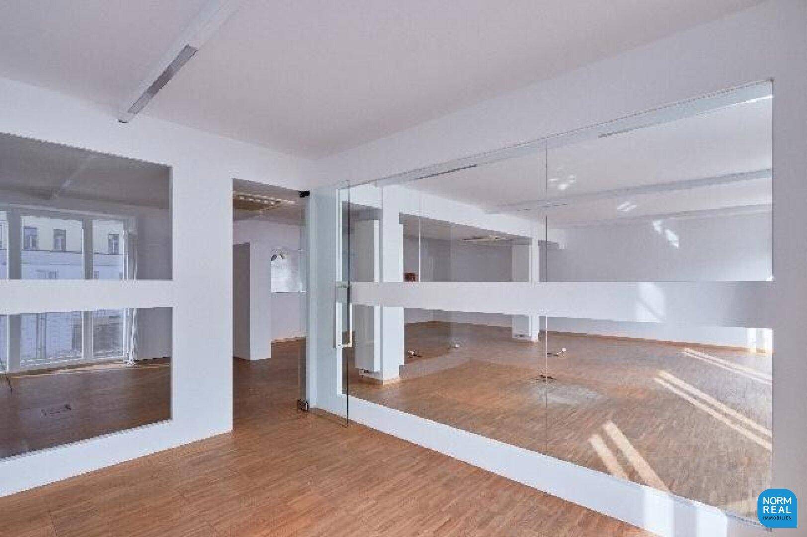 Moderner Bürobereich mit Glaswänden und Holzboden, schafft eine offene und lichtdurchflutete Arbeitsumgebung.