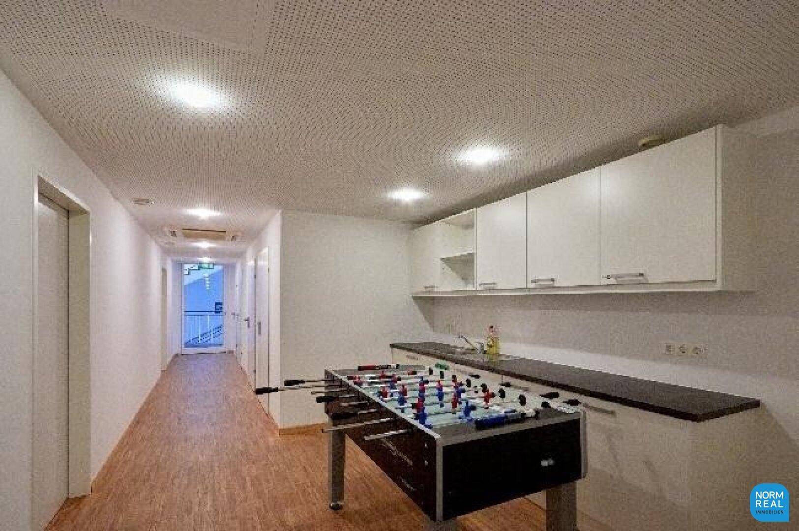 Freizeitraum mit Tischfußball und kleiner Küchenzeile, ideal für Pausen und soziale Interaktion.