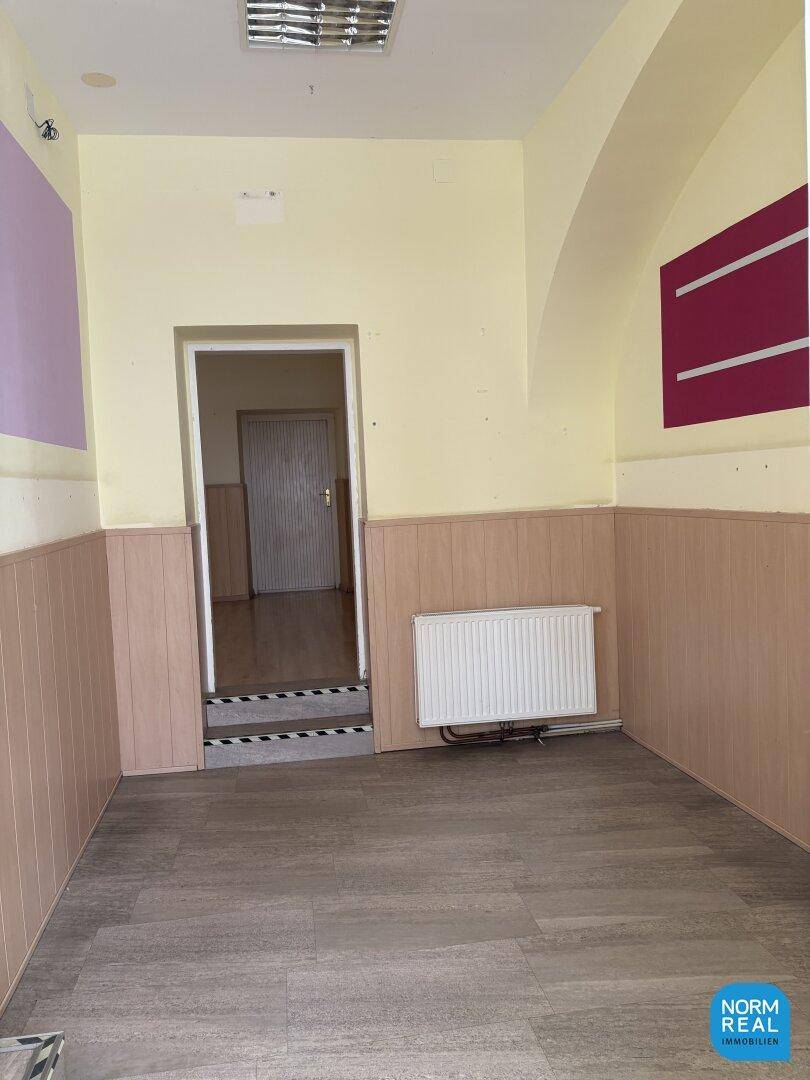Kleinerer Gewerberaum mit Laminatboden, Heizkörper und Zugang zu einem weiteren Bereich.