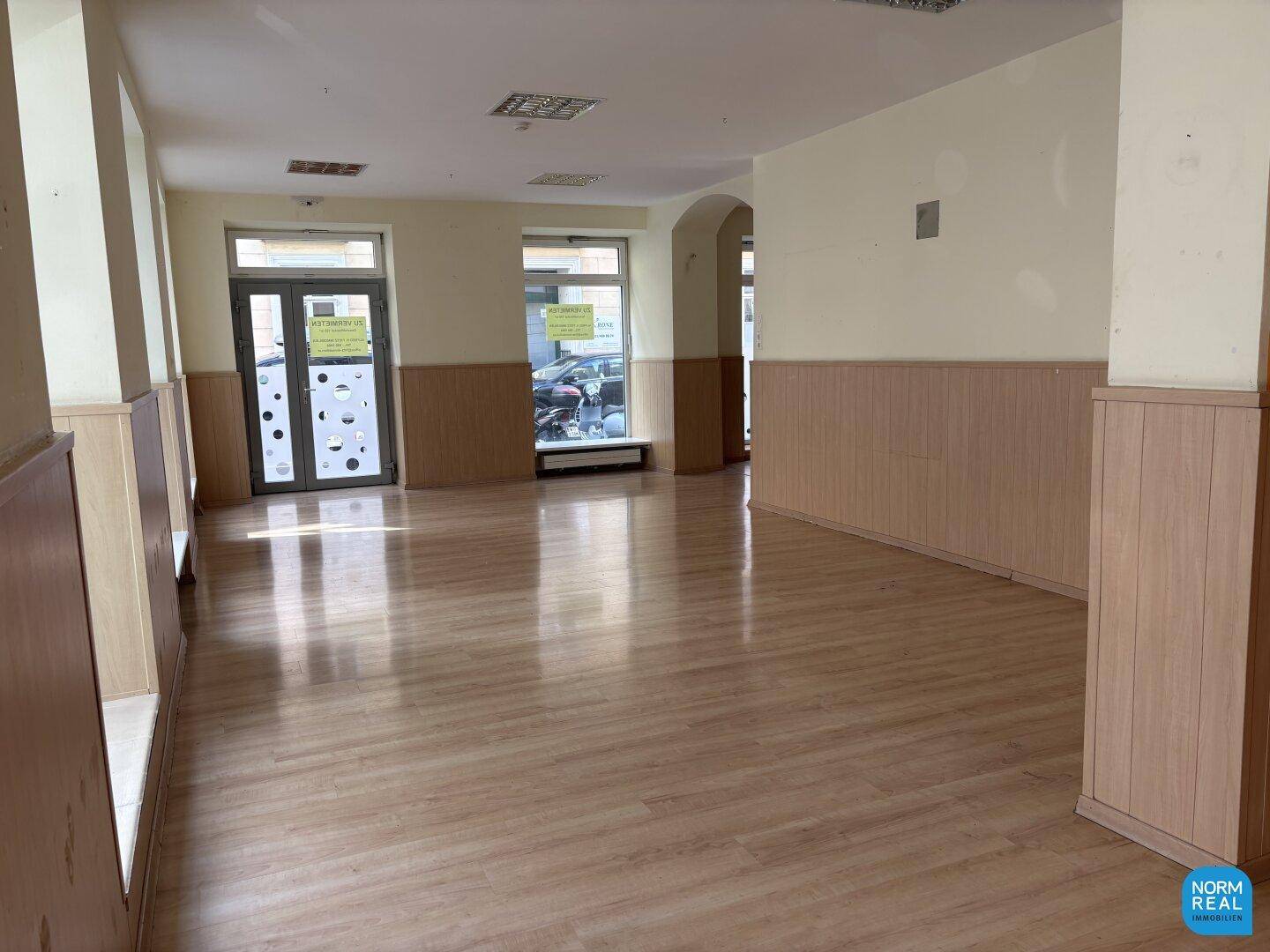 Langer Gewerberaum mit Laminatboden, großen Fenstern und viel Tageslicht.