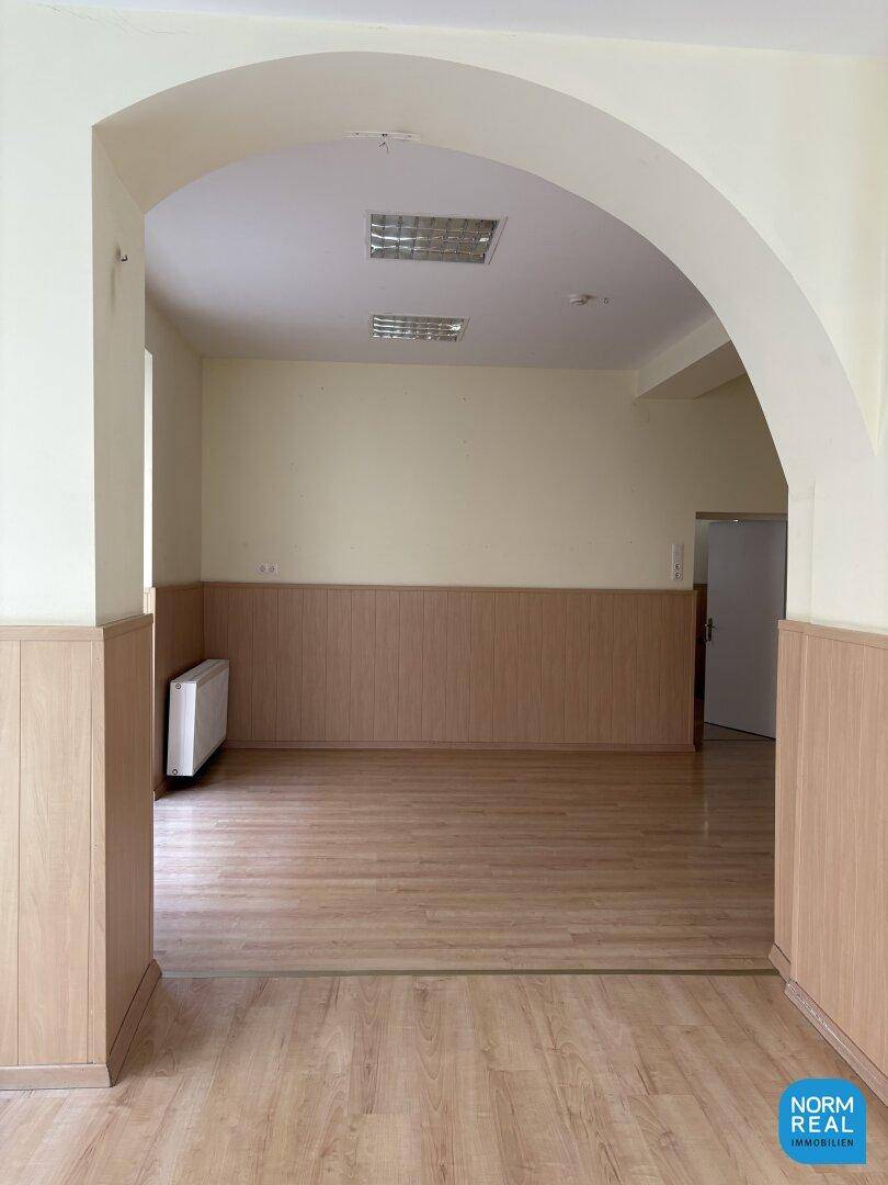 Geräumiger Gewerberaum mit einem großen Bogen und Laminatboden, gut beleuchtet.